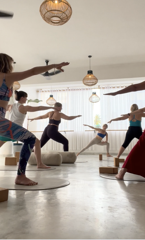 Group in warrior pose during a morning yoga class in a bright studio