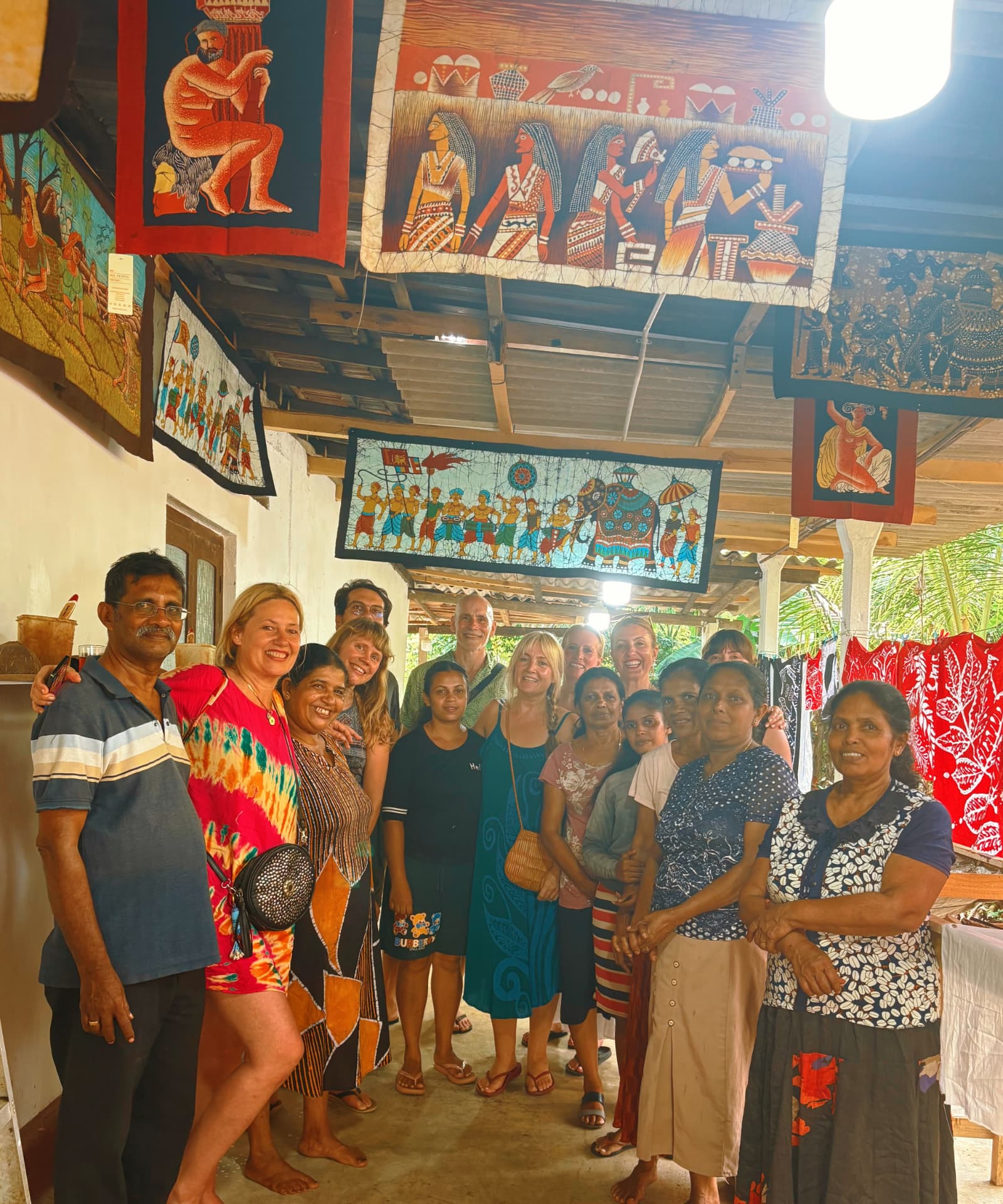 Retreat group smiling with local batik artisans beneath colourful hanging tapestries