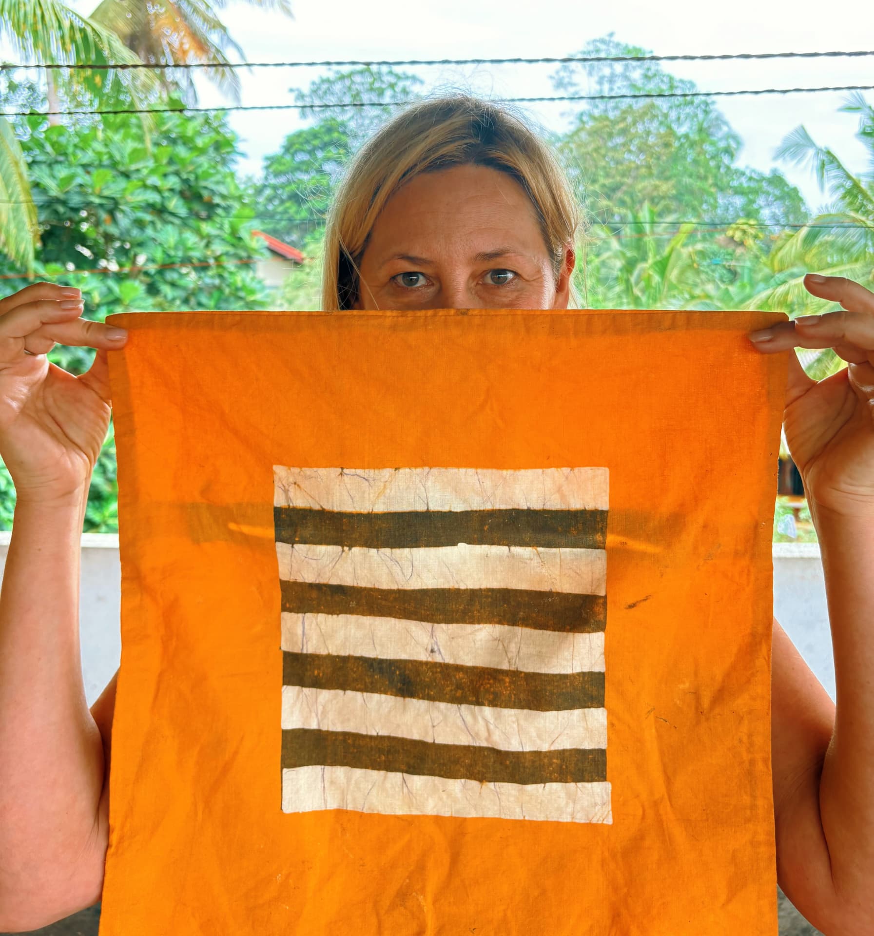 Woman holding up a hand-dyed orange batik cloth with striped pattern