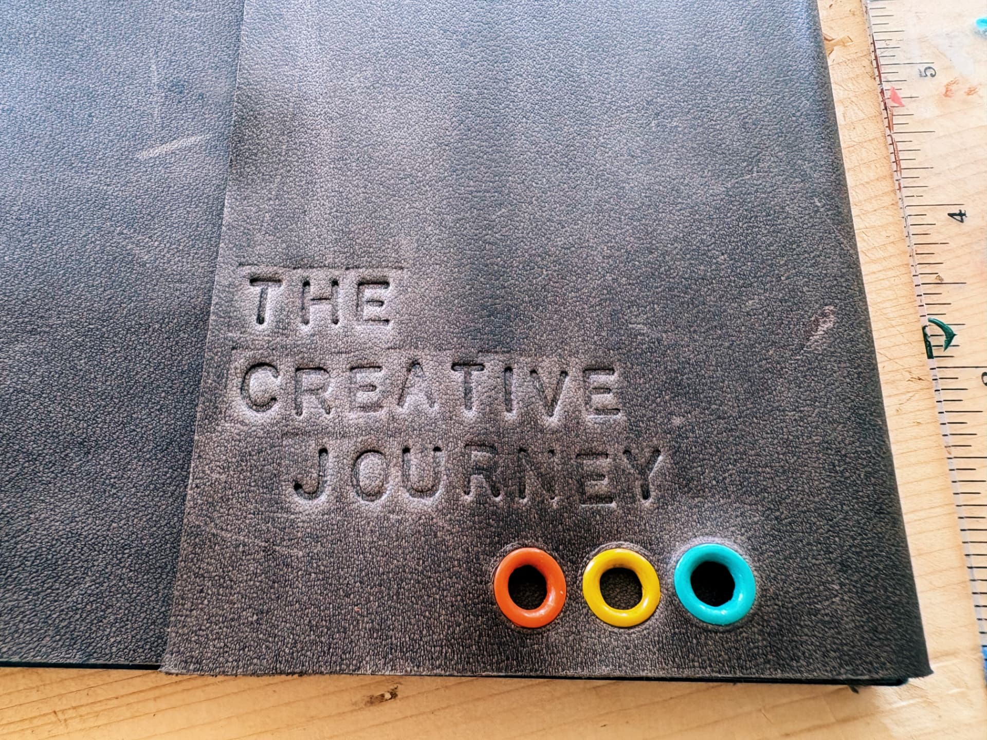 Hand-stamped leather journal reading The Creative Journey with coloured eyelets